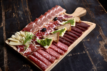 slicing of sausage and meat with croutons and olives on a wooden board