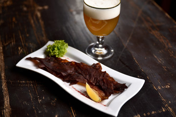 jerky with lemon and herbs on a white plate on the background of a glass of beer, basturma