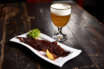 jerky with lemon and herbs on a white plate on the background of a glass of beer, basturma