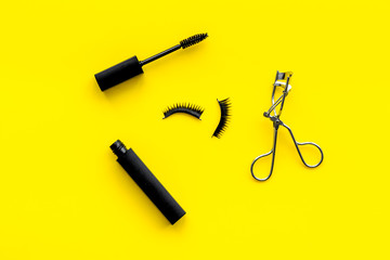decorative cosmetic set with lash curler and mascara on yellow woman desk background top view