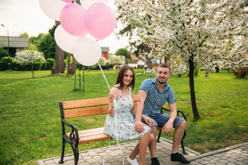 Couple siting on a bench and hold pink helium balls