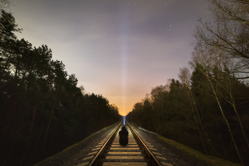Man sitting on the railway track with a flashlight pointing to the starry sky