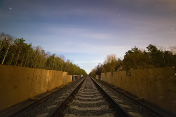 Fototapeta premium Railway track in the forest at cold starry night