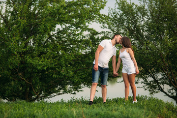 Fototapeta na wymiar Young couple in white stand on the hill. Background of trees and lake