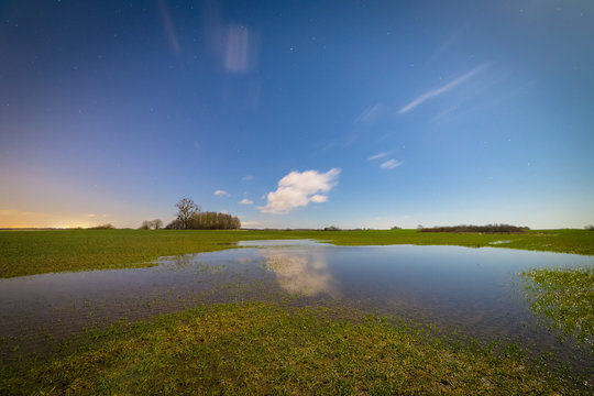 Small pond in the harvest field at night. Reflections of the sky