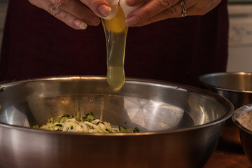 hands dropping a raw egg into a bowl with zucchini