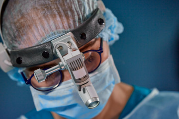Close up portrait of female surgeon doctor wearing protective mask and hat during the operation. Healthcare, medical education, surgery concept.