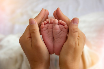 Mother Hands Holding Small Baby Feet. Close-up Tiny Baby Feet in Hands. Mother Care of Newborn Baby. Little Tiny Kid Fingers.