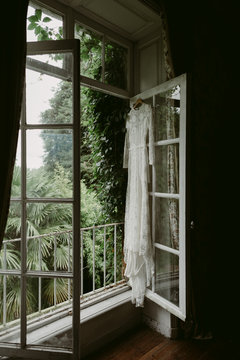 Lace wedding dress hanging in window of chateau in Normandy France
