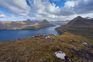 Scenic and epic landscape view from top of the one of thousand mountains in Faroe island into the deep fjord with other high cliffs and mountains in spring sunny day.