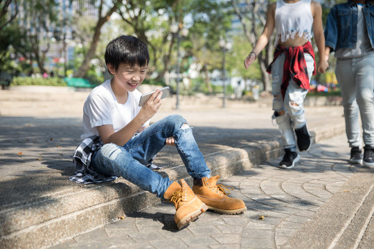 Cute boy on his phone, while two of his friends are approaching