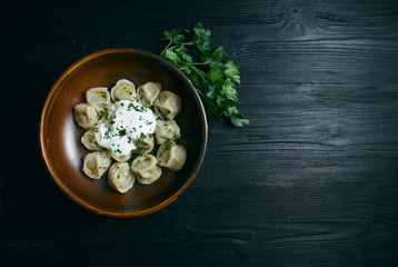 Obraz na płótnie Canvas dumplings with sour cream and greens on a black wooden table. Russian traditional dish of dough and minced meat. close up photo. Copy space.