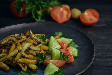 Freshly cooked fried potatoes with onions and mushrooms close-up on a plate. black wood table. horizontal view.