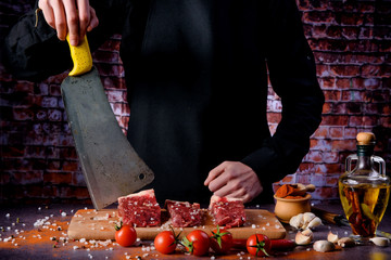 Butcher cuts fresh meat on the wood board.Beef steak and salt on background with free space for text design or logotype menu restaurant.