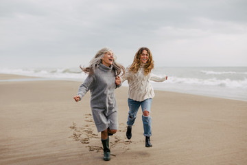 Active senior woman and her daughter enjoying on the beach in winter.