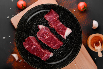 Fresh raw meat in pan with spieces,tomato,oil,salt,on a dark table, top view.