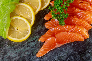 Fresh salmon fillet, lemons, avocados, parsley and spices on marble cutting board
