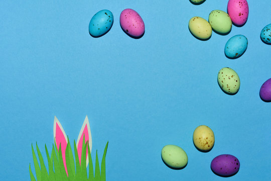 Candy Eggs On Blue With Grass Patch And Rabbit Ears