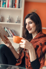 Young beautiful woman reading a book at home, enjoying a cup of coffee and good read