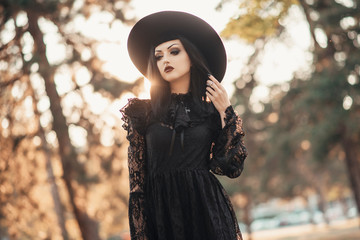 Dark gothic witch in black attire walking in the woods