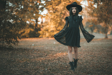 Dark gothic witch in black attire walking in the woods