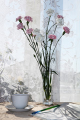 Flowers in a vase and a cup of coffee on a sunny window in a rustic house on a wooden table, a beautiful light background of early morning and good mood, long shadows from flowers and a window
