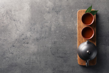 Board with cups and teapot of freshly brewed oolong on grey background, top view with space for text