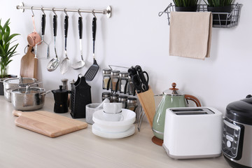 Set of clean cookware, dishes, utensils and appliances on table at white wall