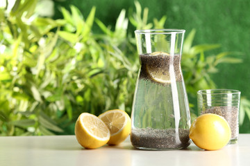 Glass and jug of lemon water with chia seeds on table. Space for text