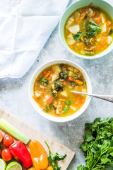 Minestrone soup, on bowl and jar with vegetables cut on a cutboard cherry tomato brown, lime,  on a concrete white backround