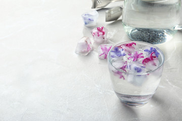 Glass of water with floral ice cubes on table. Space for text