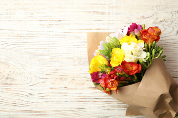 Bouquet of beautiful spring freesia flowers on wooden background, top view. Space for text