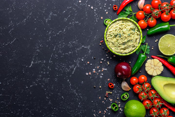 Traditional Mexican Latin American sauce Guacamole and ingredients on black stone table. Top view copy space.