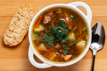 Lentil soup with chicken in a white bowl on a wooden board, top view