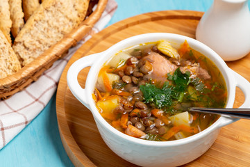 Lentil soup with chicken in a white bowl on a wooden board on a blue table
