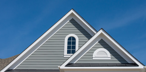 White attic window vent, gable, corbel, louver on a new construction luxury American single family home in the East Coast USA with blue sky background