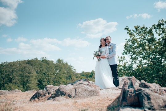 Wedding photo of the bride and groom in a gray-pink color on nature in the forest and rocks.