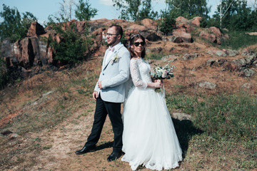 Wedding photography fashionable bride and groom in sunglasses on the nature on the rocks.