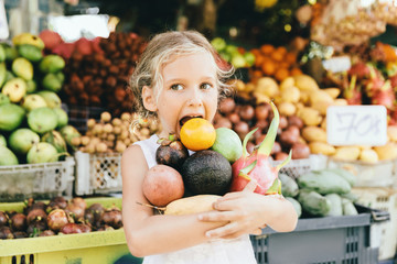 The child holding a bunch of fruits in the fruit store