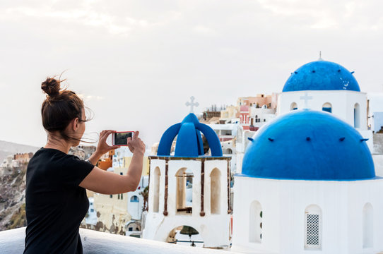 Tourist woman taking photos on the streets of Oia in Santorini, Greece