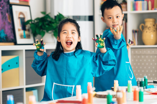 Preschool kids in smock showing finger paint on hands in classroom