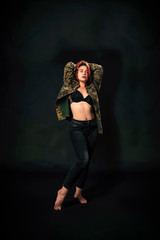 beautiful young girl with red hair and in army jacket on black background.