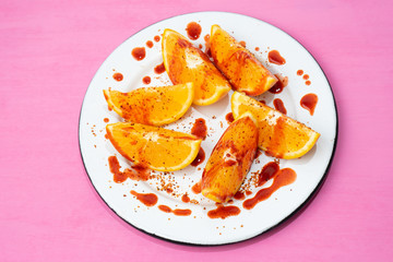 Orange slices with chilli powder and chamoy on colorful background