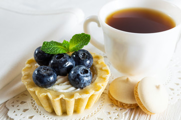 Delicious tartlet with fresh blueberries and cream cheese, a сup of tea and small cookies.
