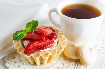 Delicious tartlet with fresh strawberries and cream cheese, a сup of tea and small cookies.