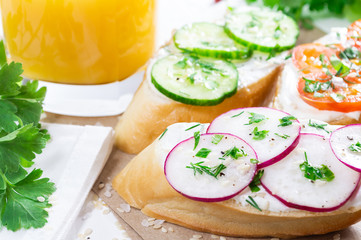 Healthy breakfast: sandwiches with cream cheese and vegetables, and orange juice on a light background.