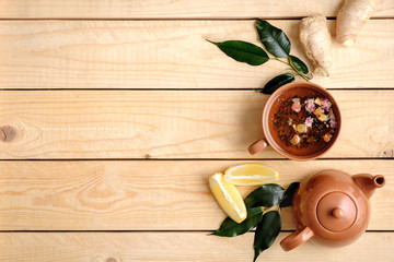 Cup of herbal tea, teapot, lemon, plants leaves and ginger root on rustic wooden background, view from above, flat lay composition with copy space