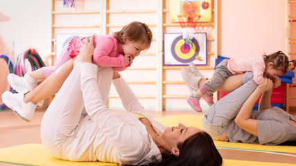 Babies have fun pastime while mothers doing workout in gym class to loose extra weight....
