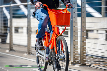 Man rides an orange bike with basket on bike path