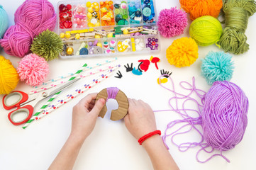 The child is engaged in a favorite hobby. The kid makes a pom-pom from a woolen thread monster. Holiday toy gift.